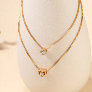 Este colar em camadas é um adorno encantador que apresenta um pingente em forma de coração. Com várias camadas que se entrelaçam de forma graciosa, este acessório adiciona um toque de romance e estilo ao seu visual. Perfeito para expressar amor e elegância em qualquer ocasião.