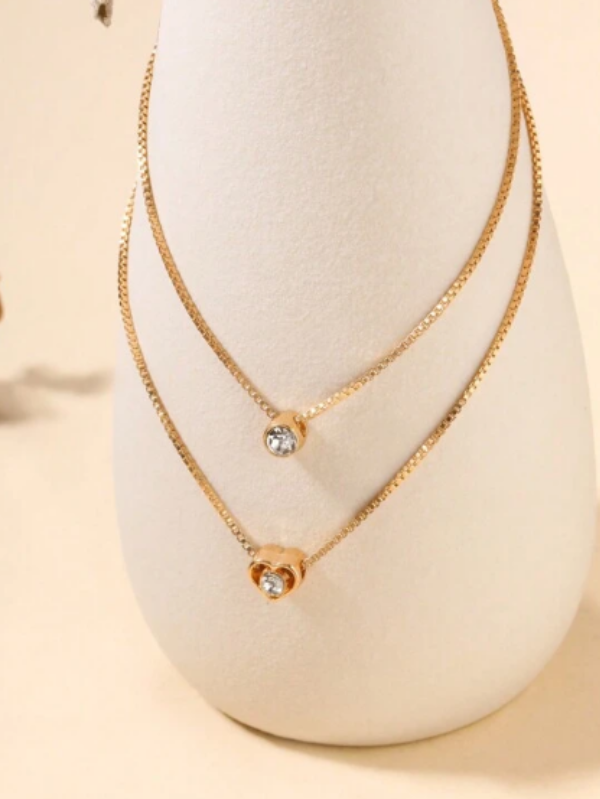 Este colar em camadas é um adorno encantador que apresenta um pingente em forma de coração. Com várias camadas que se entrelaçam de forma graciosa, este acessório adiciona um toque de romance e estilo ao seu visual. Perfeito para expressar amor e elegância em qualquer ocasião.